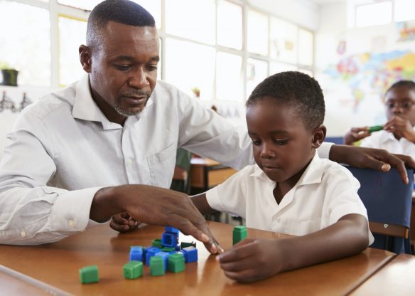 Teacher helping elementary school boy counting with blocks